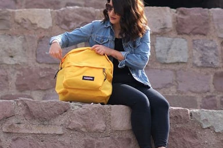 A woman sits on a historic stone wall in Ankara, checking her backpack on a sunny day.